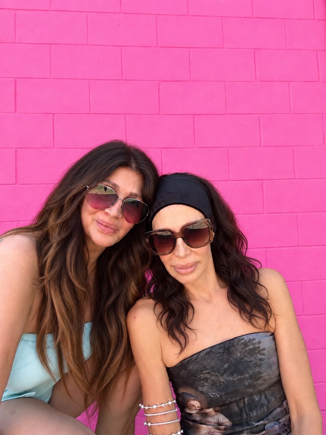 Beth and Te-see Bender in sunglasses, leaning their heads together against a pink wall